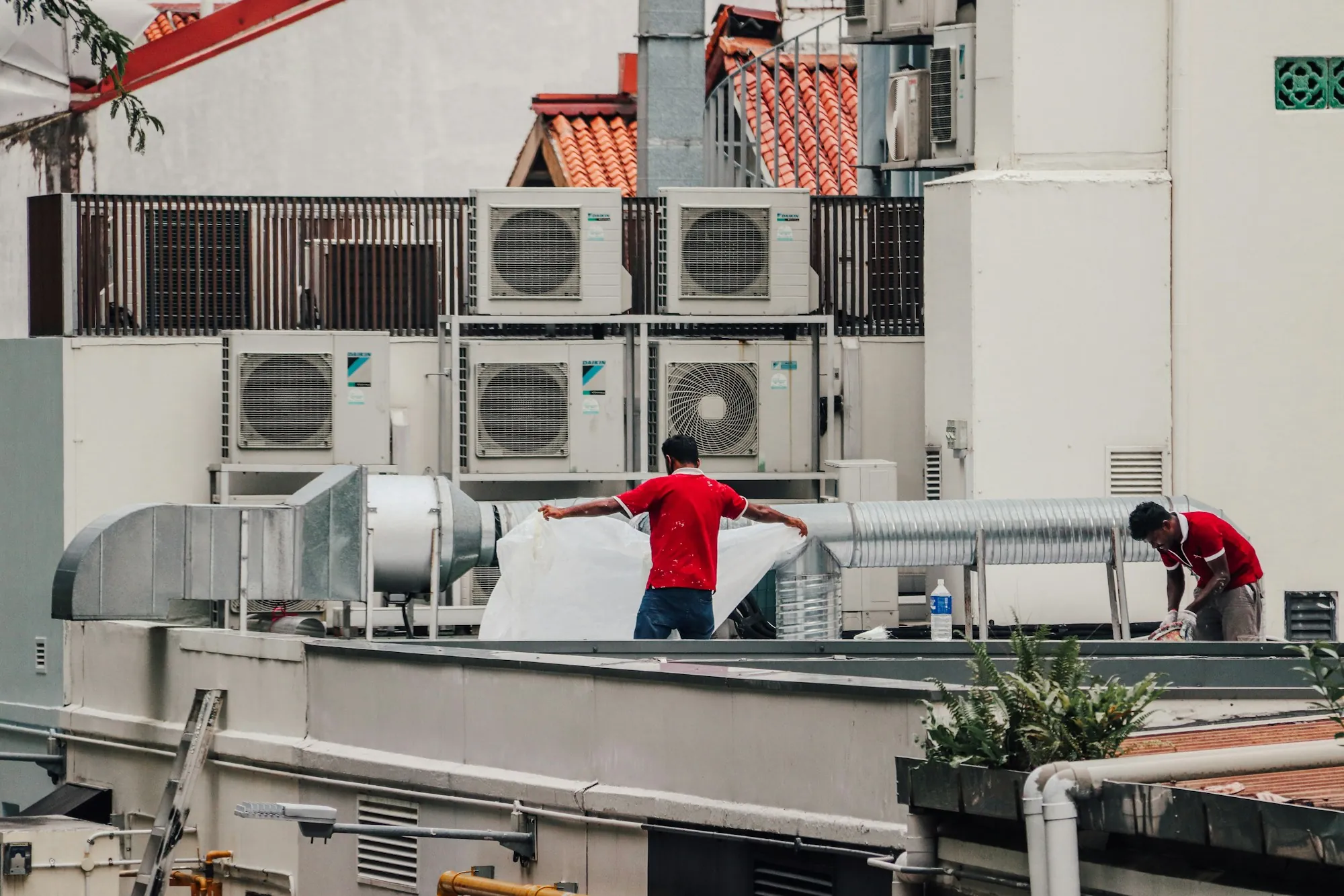 Workers on a rooftop among commercial condensers and ducts